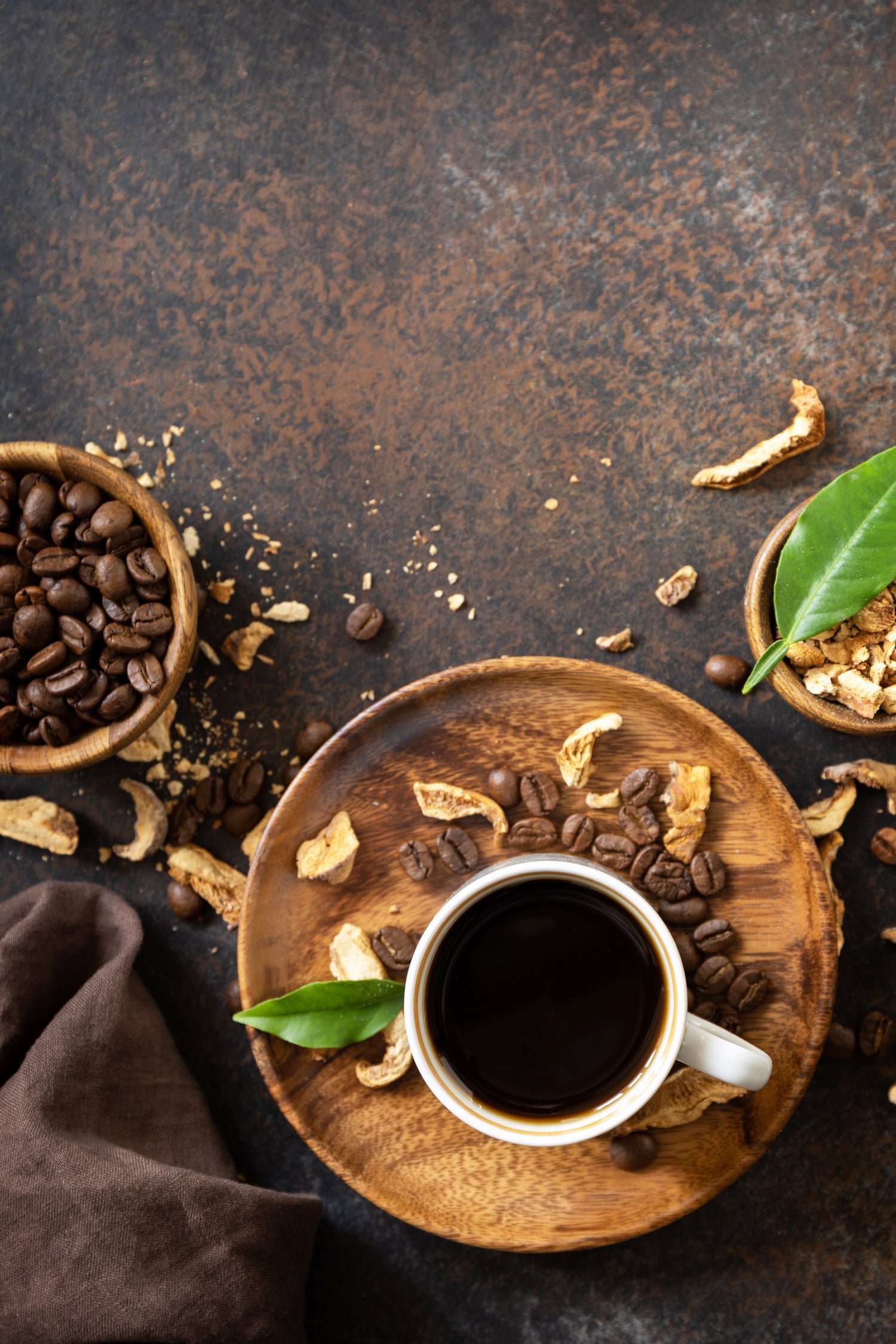 Cup of bold coffee roasts on a wooden plate surrounded by coffee beans and green leaves